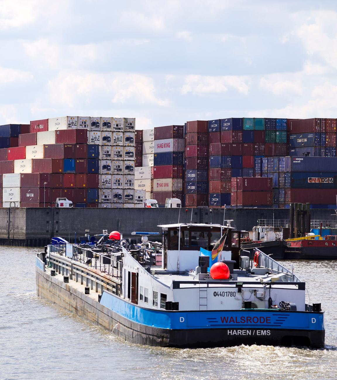 Ein kleines Frachtschiff fährt durch einen Kanal im Hamburger Hafen. Im Hintergrund lagern Container.