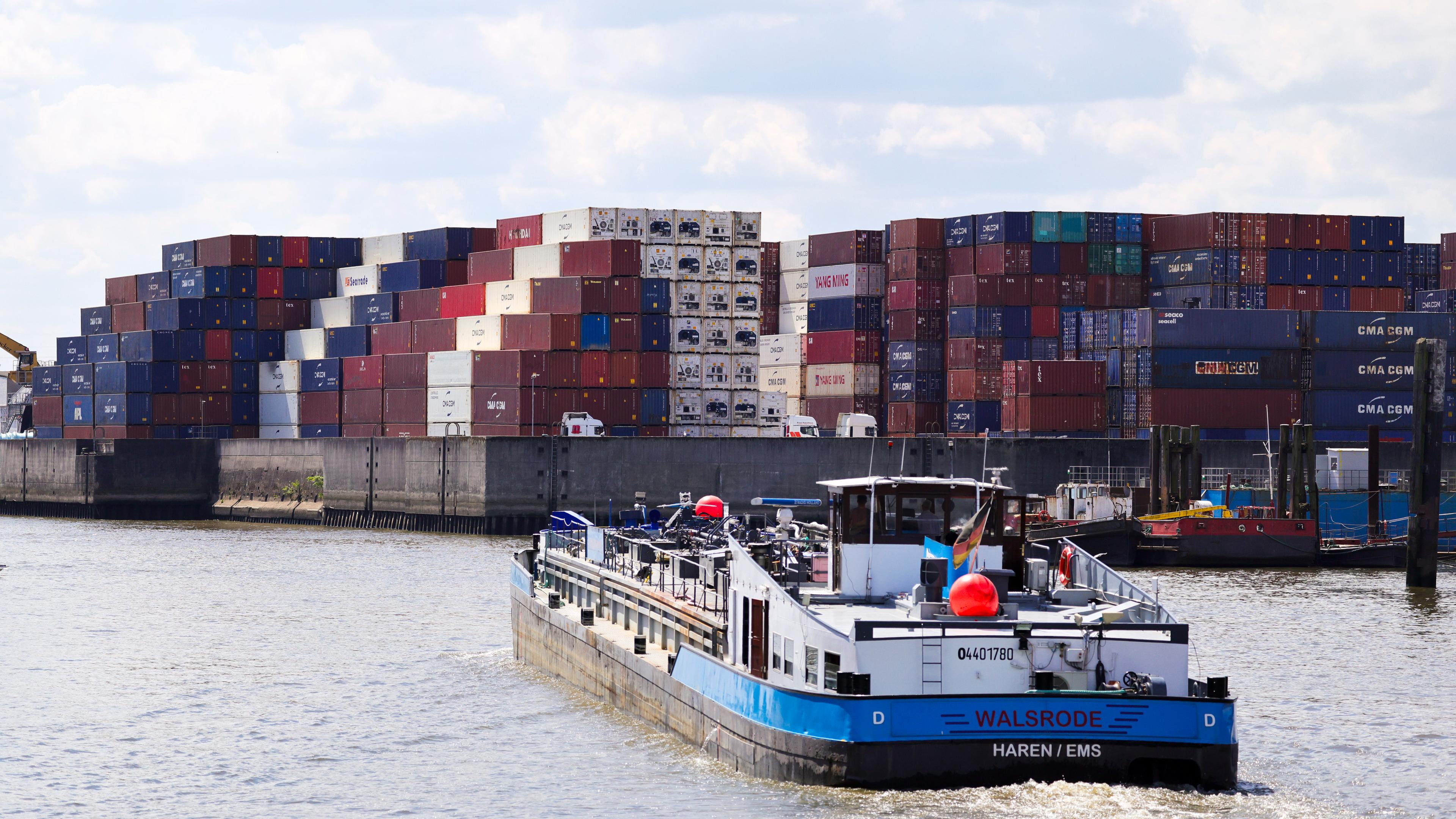 Ein kleines Frachtschiff fährt durch einen Kanal im Hamburger Hafen. Im Hintergrund lagern Container.