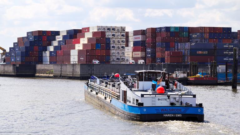 Ein kleines Frachtschiff fährt durch einen Kanal im Hamburger Hafen. Im Hintergrund lagern Container.