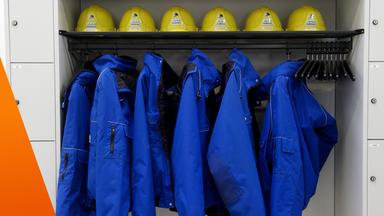 Ein Schrank mit blauen Arbeitsanzügen und oben drüber ein Fach mit Helmen