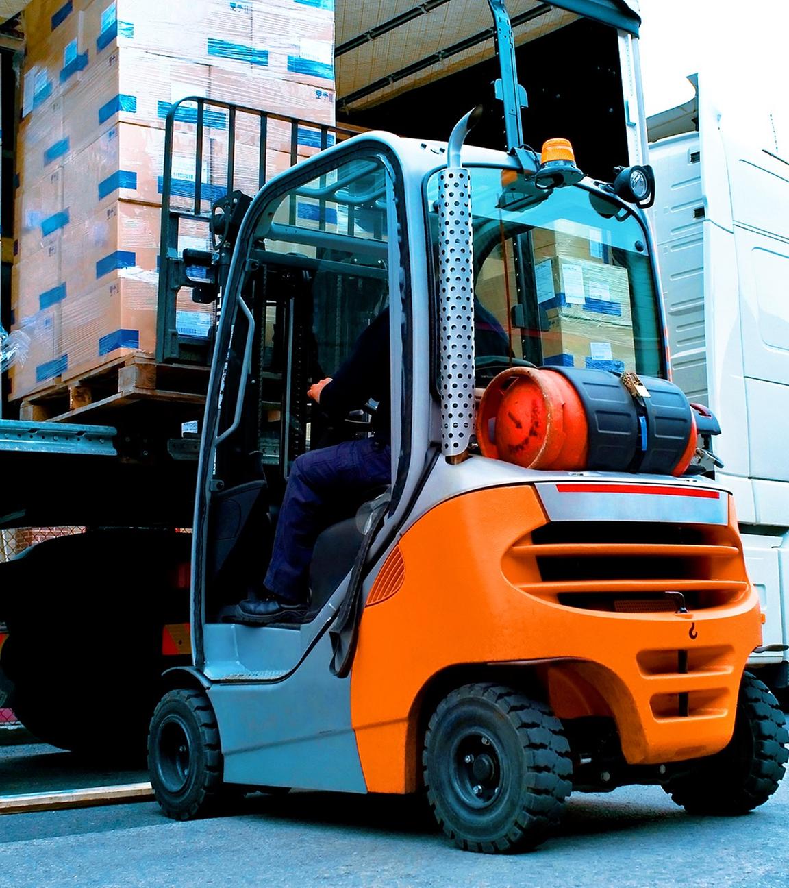Große Lagerhalle mit Hochregalen. Ein Gabelstapler belädt einen LKW mit Paletten.
