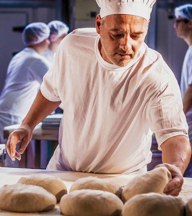 Ein Bäcker formt aus Teig Brote