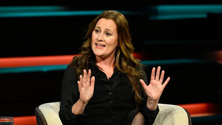 Janine Wissler in schwarzer Bluse sitzt sprechend und mit beiden Händen gestikulierend auf Stuhl im Lanz-Studio.