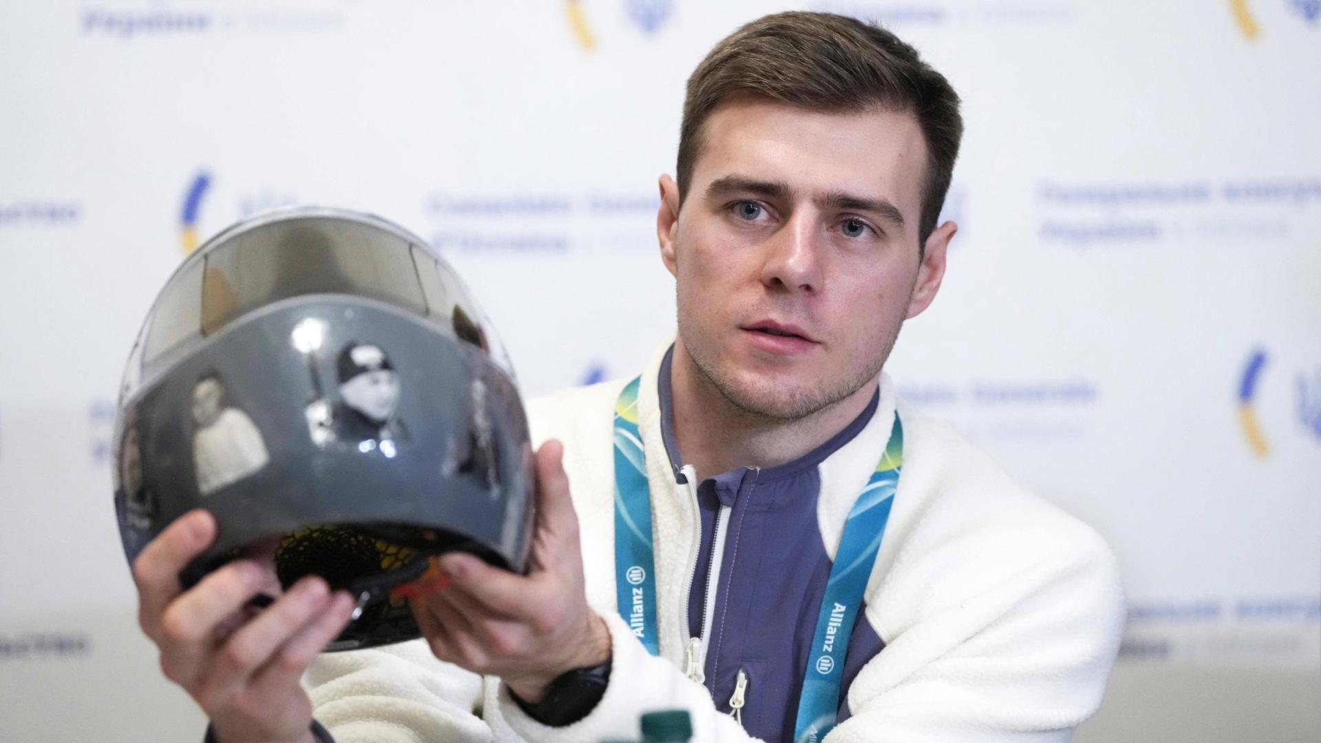 Der ukrainische Skeletonfahrer Wladyslaw Heraskewytsch zeigt bei einer Pressekonferenz zu den Olympische Winterspielen 2026 seinem Helm mit Erinnerungsbildern von getöteten ukrainischen Sportlern