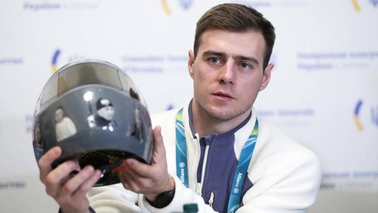 Der ukrainische Skeletonfahrer Wladyslaw Heraskewytsch zeigt bei einer Pressekonferenz zu den Olympische Winterspielen 2026 seinem Helm mit Erinnerungsbildern von getöteten ukrainischen Sportlern