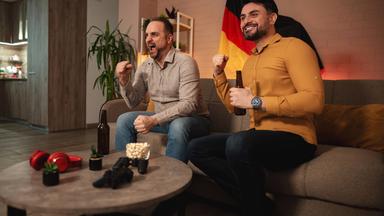Zwei Fußball-Fans feiern zu Hause vor dem Fernseher im Wohnzimmer.