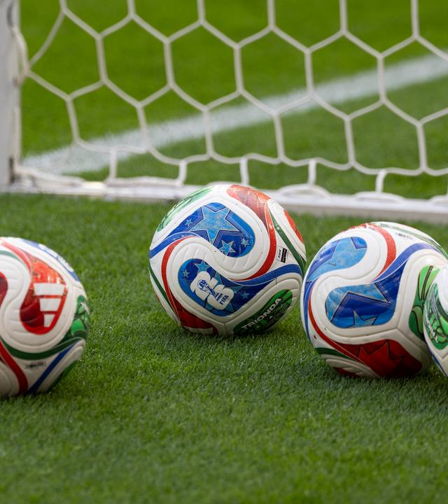 5 Adidas Baelle (Ball) Trionda fuer die Fussball WM 2026, auf dem Rasen liegend, vor dem Tornetz