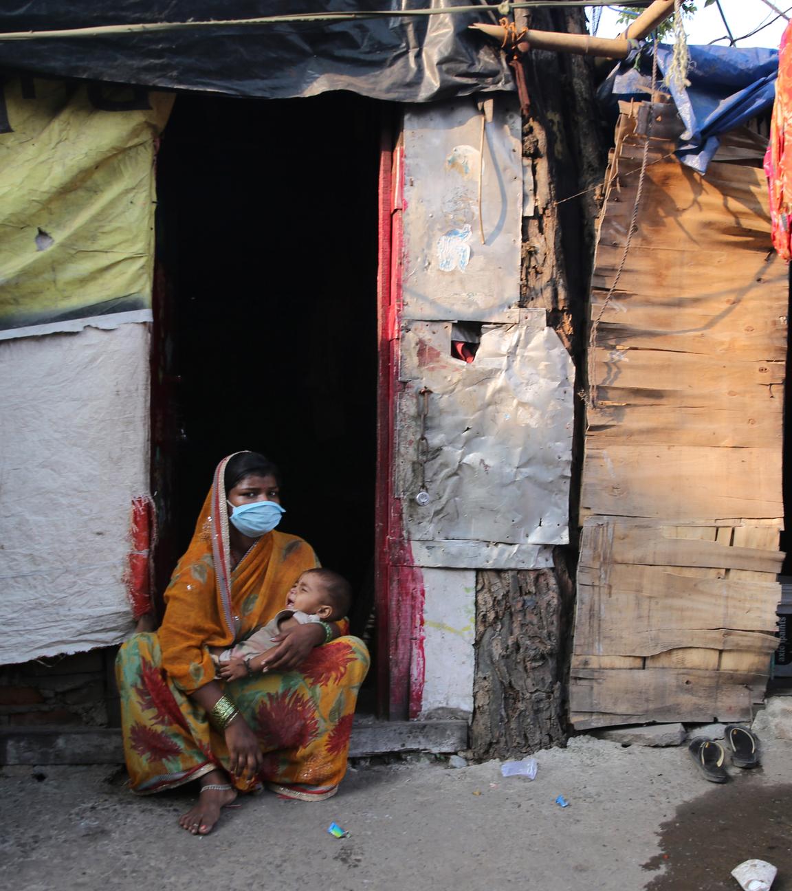 Auf dem Bild ist eine Frau mit ihrem Baby zu sehen in einem Slum in Neu-Dehli.