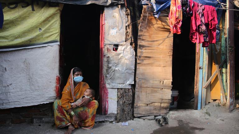 Auf dem Bild ist eine Frau mit ihrem Baby zu sehen in einem Slum in Neu-Dehli.