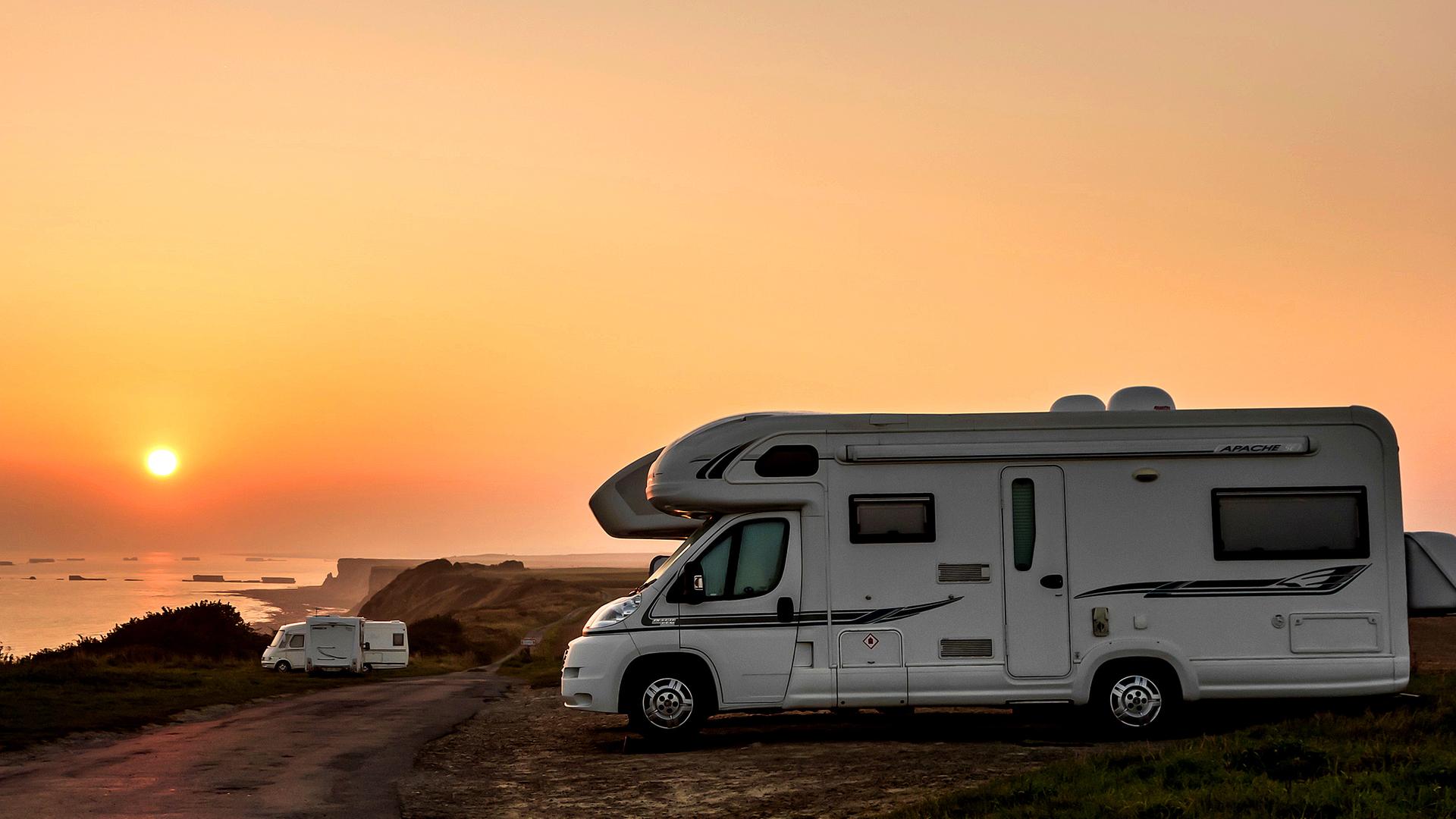 Wohnmobil an Küstenlandschaft vor untergehender Sonne.