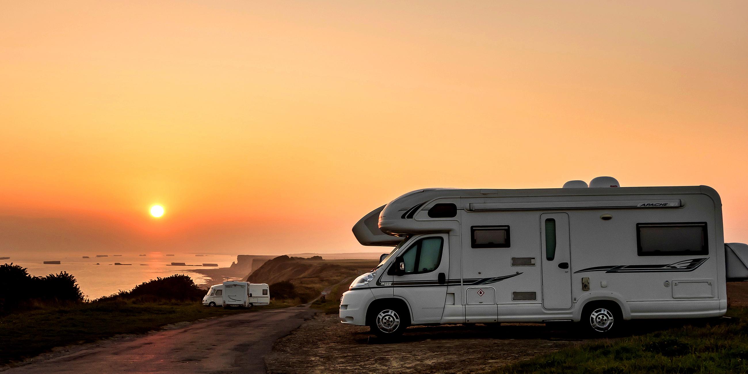 Wohnmobil an Küstenlandschaft vor untergehender Sonne.