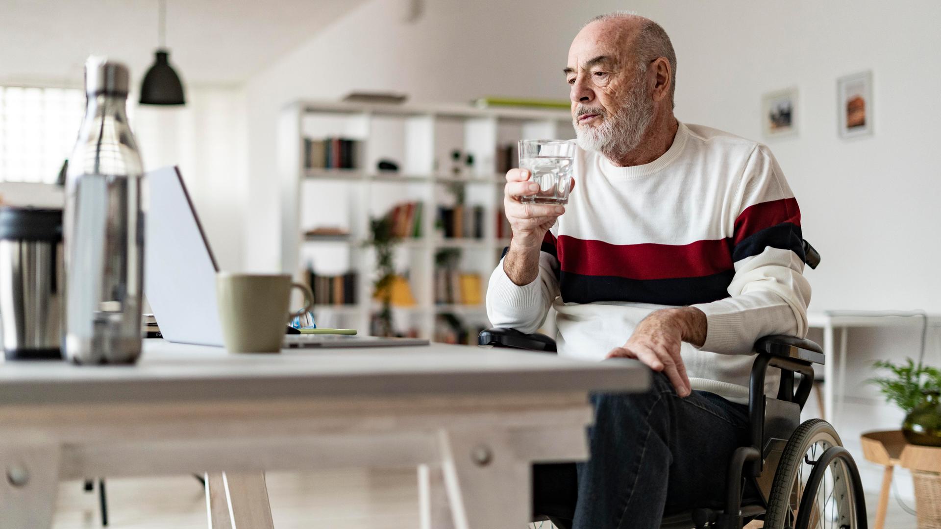 Ein Mann im Rollstuhl sitzt an einem Tisch und blickt auf einen Laptop.