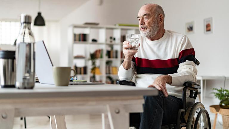 Ein Mann im Rollstuhl sitzt an einem Tisch und blickt auf einen Laptop.