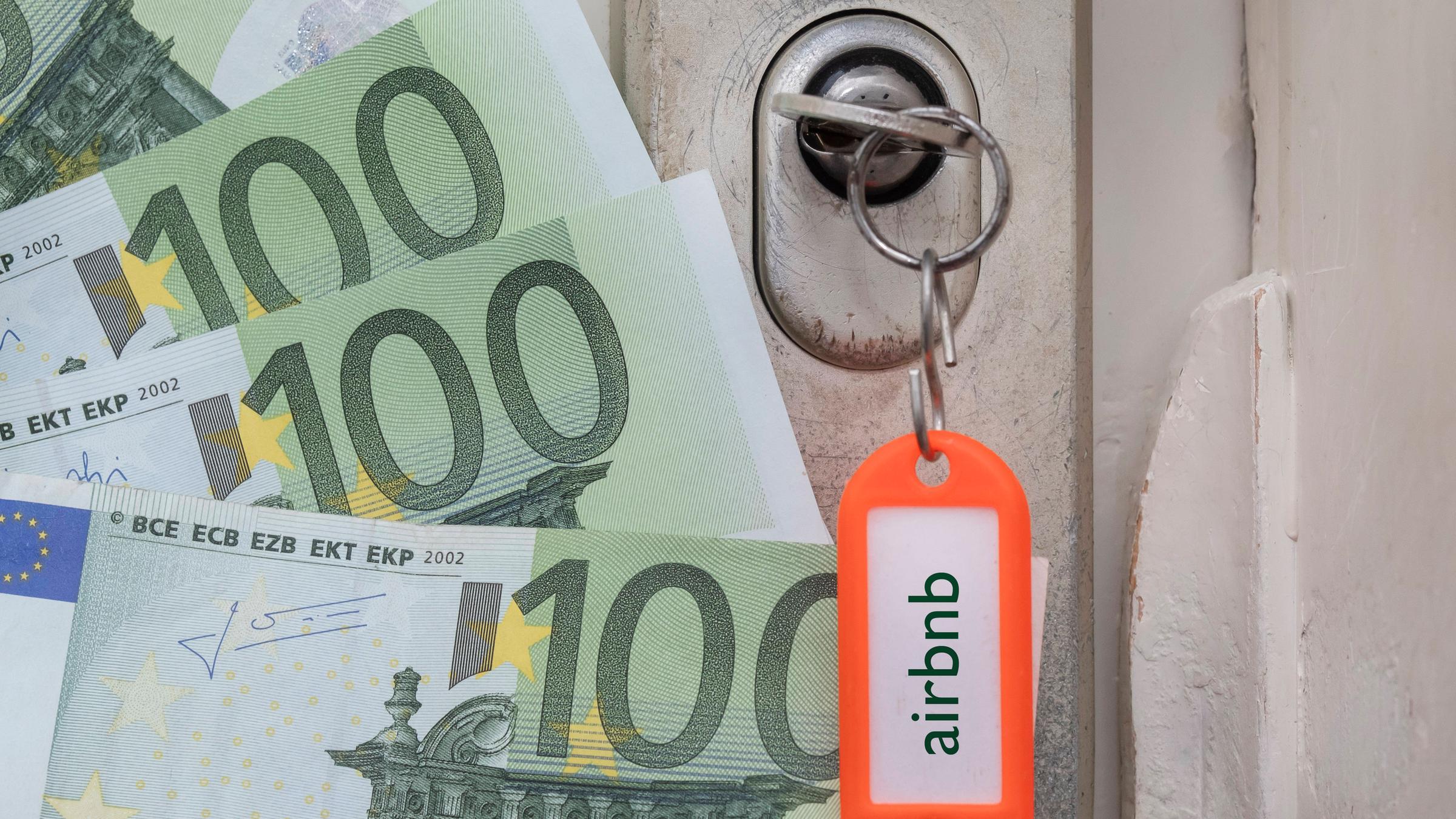 Ein Schlüssel steckt im Türschloss, am Anhänger prangt der Schriftzug Airbnb, daneben liegen Euro-Scheine.
