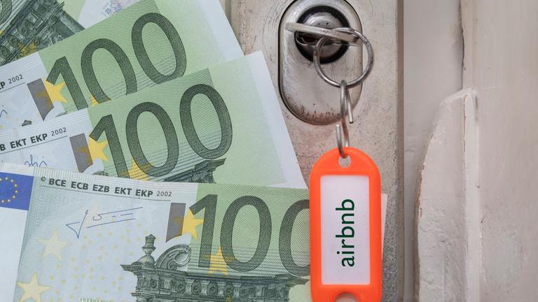Ein Schlüssel steckt im Türschloss, am Anhänger prangt der Schriftzug Airbnb, daneben liegen Euro-Scheine.