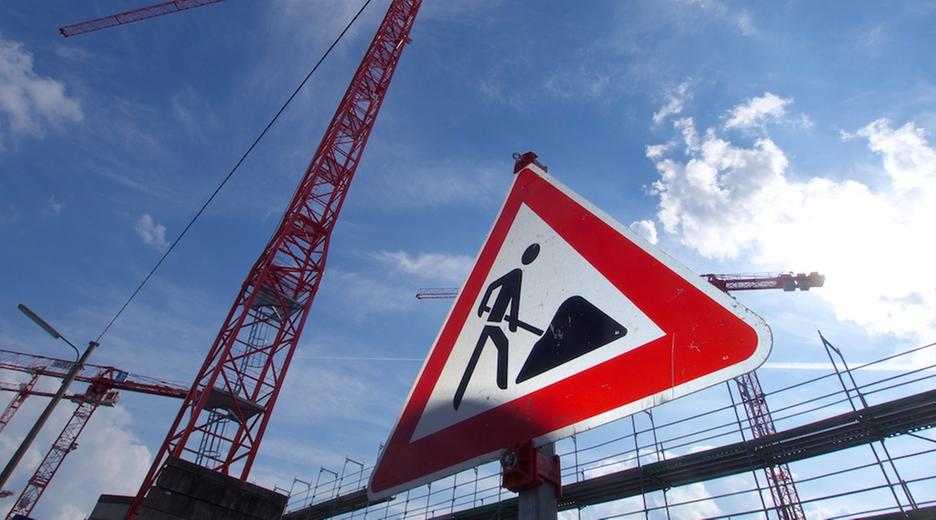 Bayern, München: Ein Baustellenschild und Baukräne stehen im Münchner Stadtteil Freiham. 
