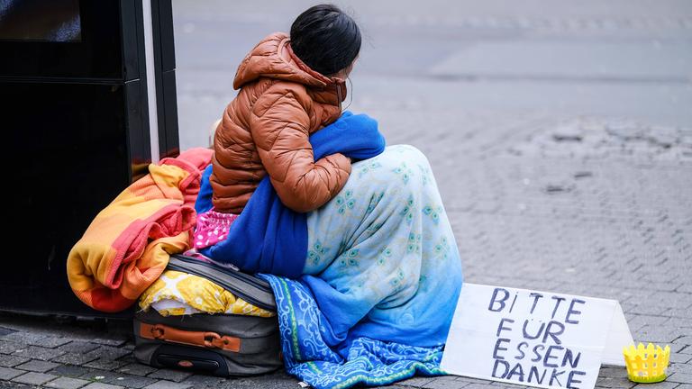 Obdachlose Person auf der Straße, sitzt mit Rücken zur Kamera.