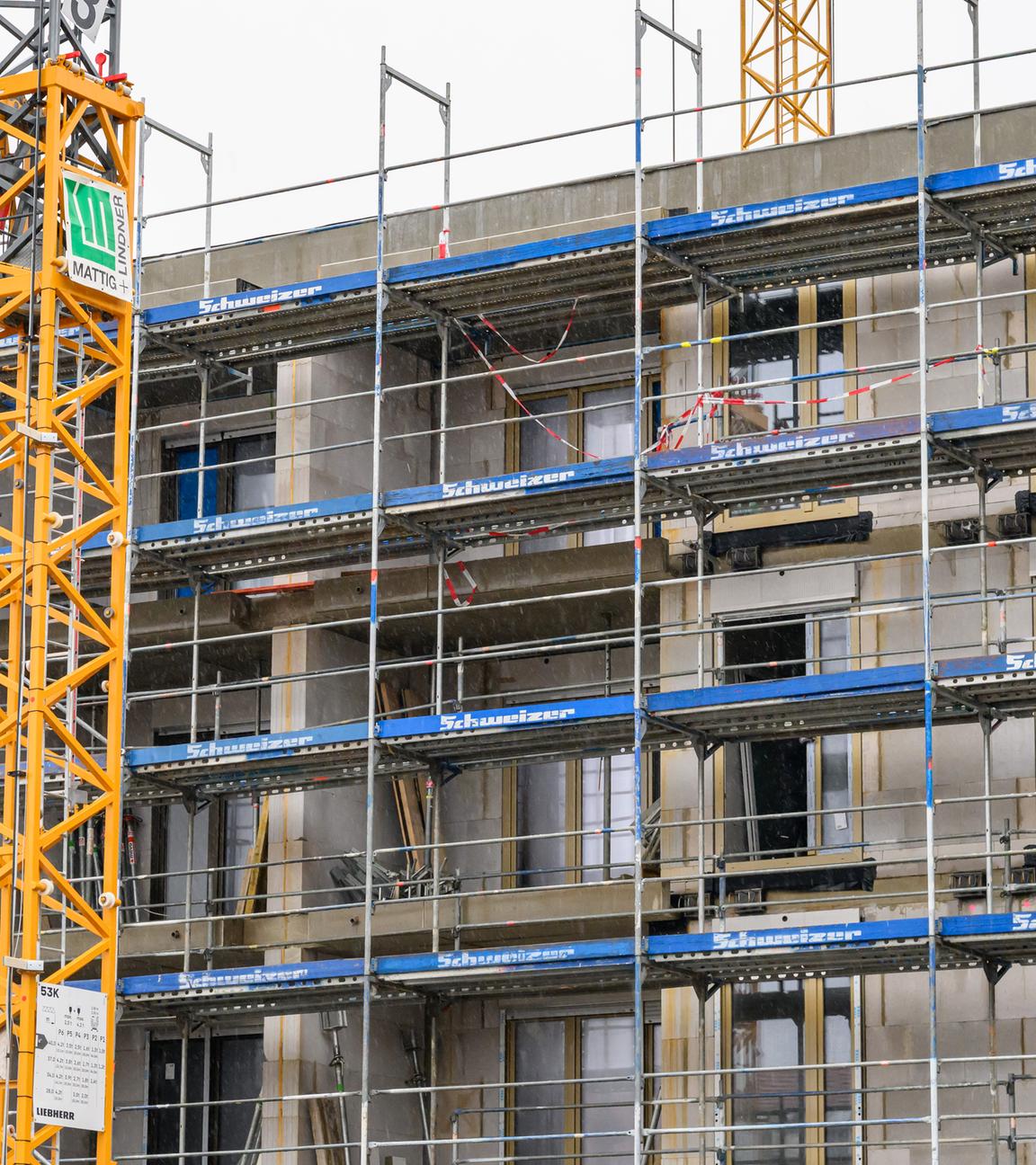 Symbolbild:  An einem im Bau befindlichen Gebäude des sozialen Wohnungsbaus sind Fassadenelemente montiert, das Haus ist von einem Baugerüst umgeben