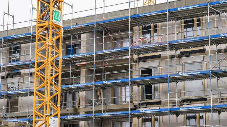 Symbolbild:  An einem im Bau befindlichen Gebäude des sozialen Wohnungsbaus sind Fassadenelemente montiert, das Haus ist von einem Baugerüst umgeben