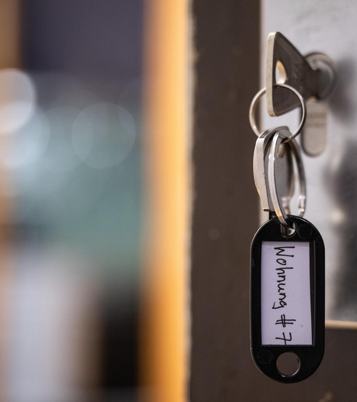 Symbolbild: Ein Schlüssel mit der Aufschrift «Wohnung #7» hängt an einer Wohnungseingangstür.