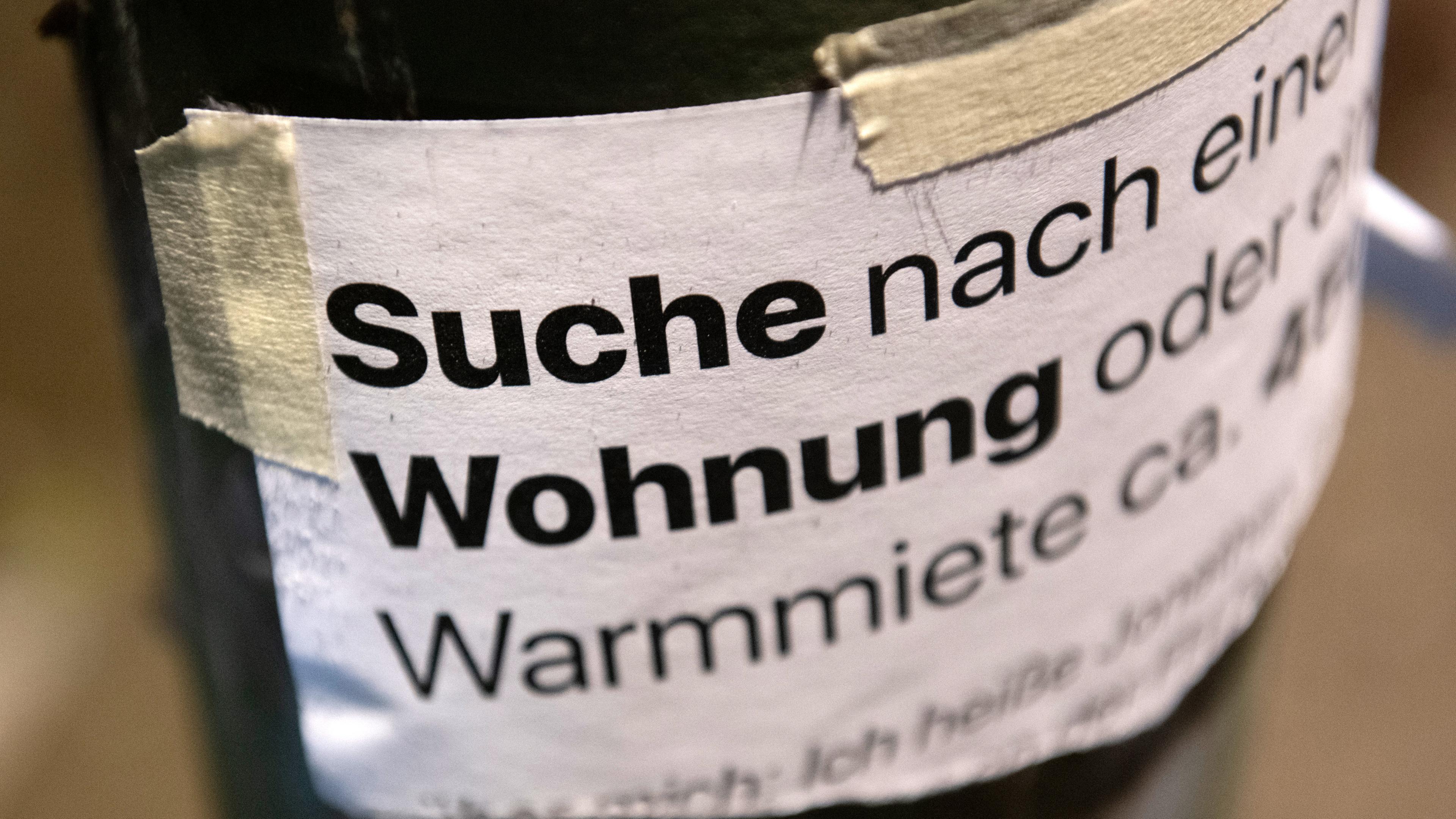 Ein Zettel mit der Aufschrift "Suche Wohnung" hängt an einer Laterne an Laterne zur Wohnungssuche