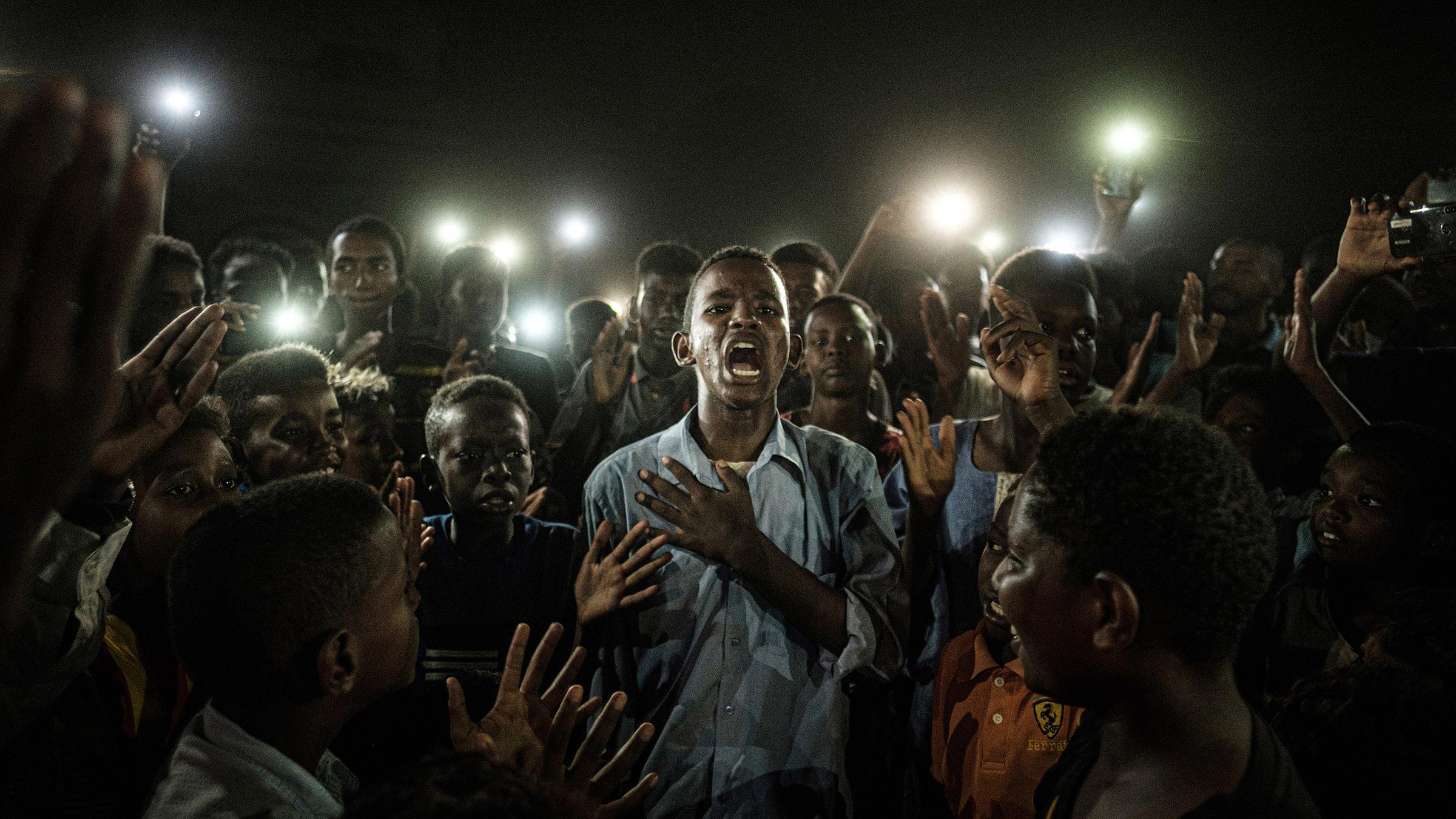Sudan, Khartoum: World press photo of the year: Ein junger Mann rezitiert mitten in einer Gruppe von Demonstranten und im Schein vieler Handylampen Gedichte.