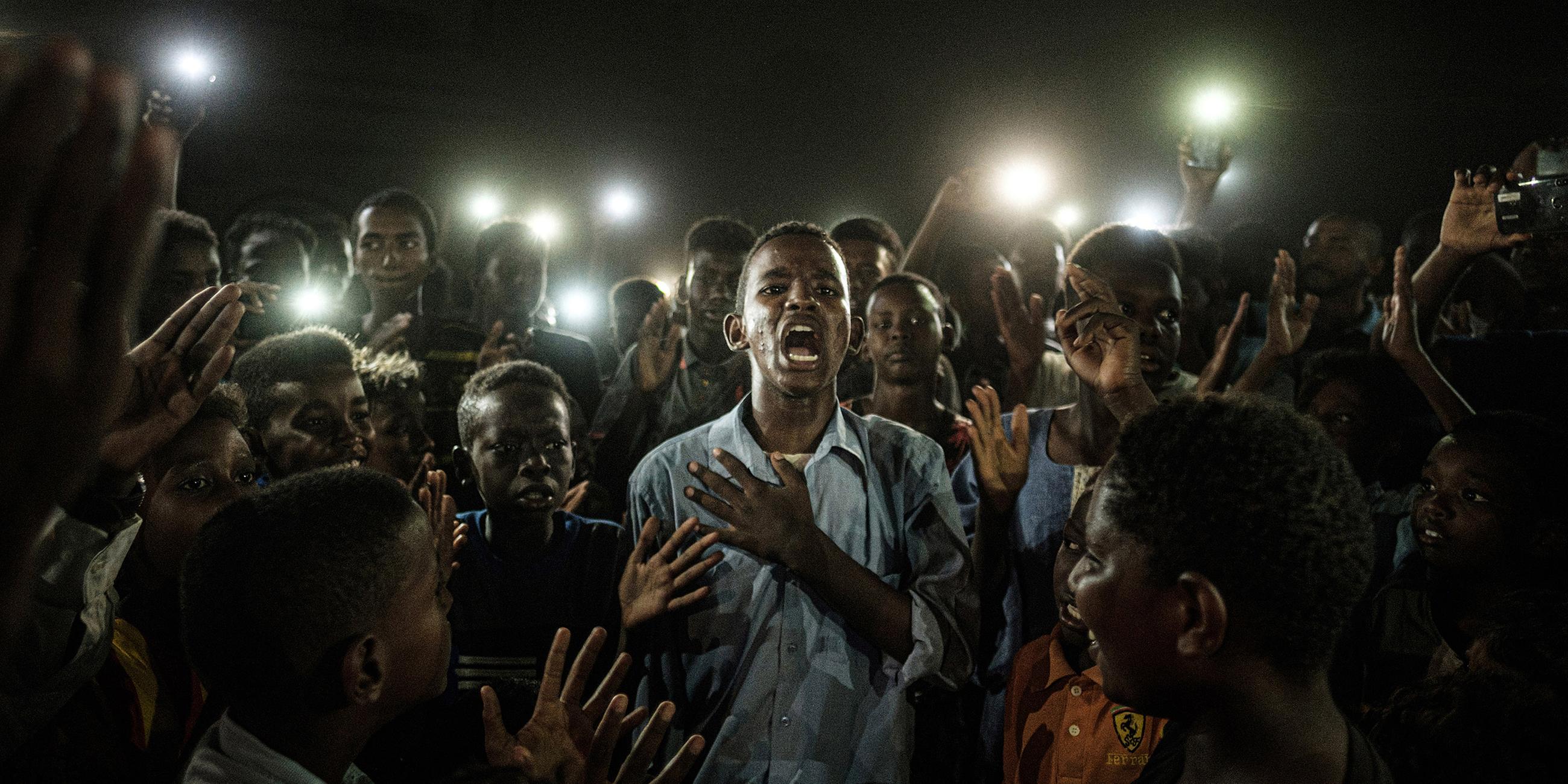 Sudan, Khartoum: World press photo of the year: Ein junger Mann rezitiert mitten in einer Gruppe von Demonstranten und im Schein vieler Handylampen Gedichte.