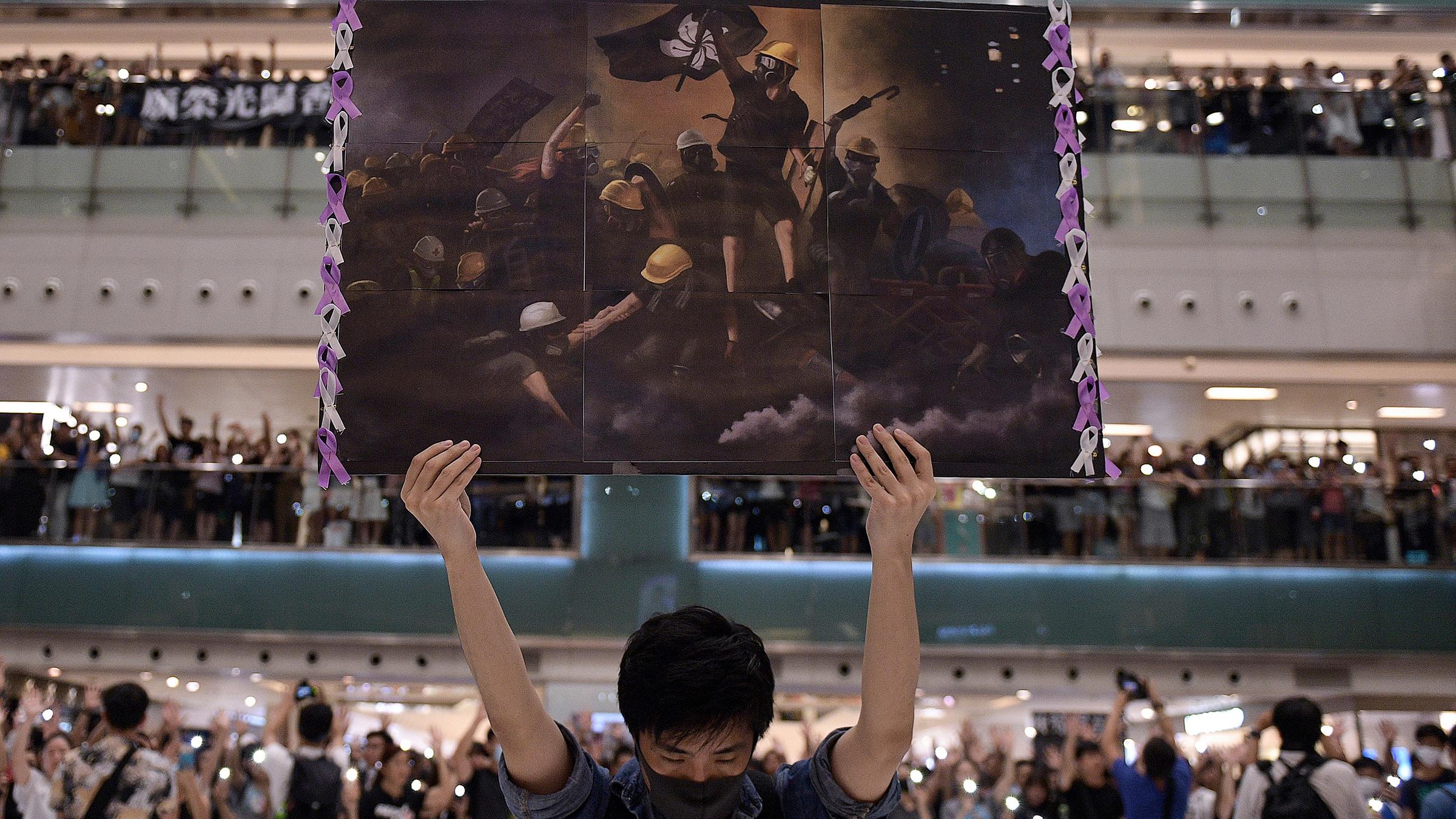 Hongkong, Shatin: Ein Mann hält ein Plakat in der Hand, während sich die Menschen zum singen von 'Glory to Hong Kong' versammelt haben.