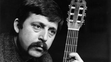 Wolf Biermann. Er blickt zur Seite und hält seine Gitarre.