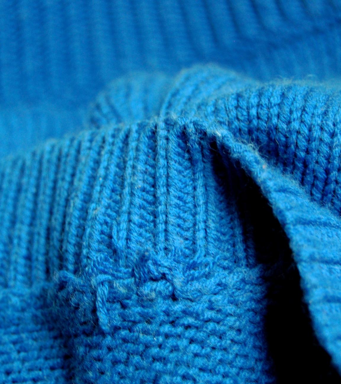 Ein blauer Strickpullover liegt in Falten im Bild.