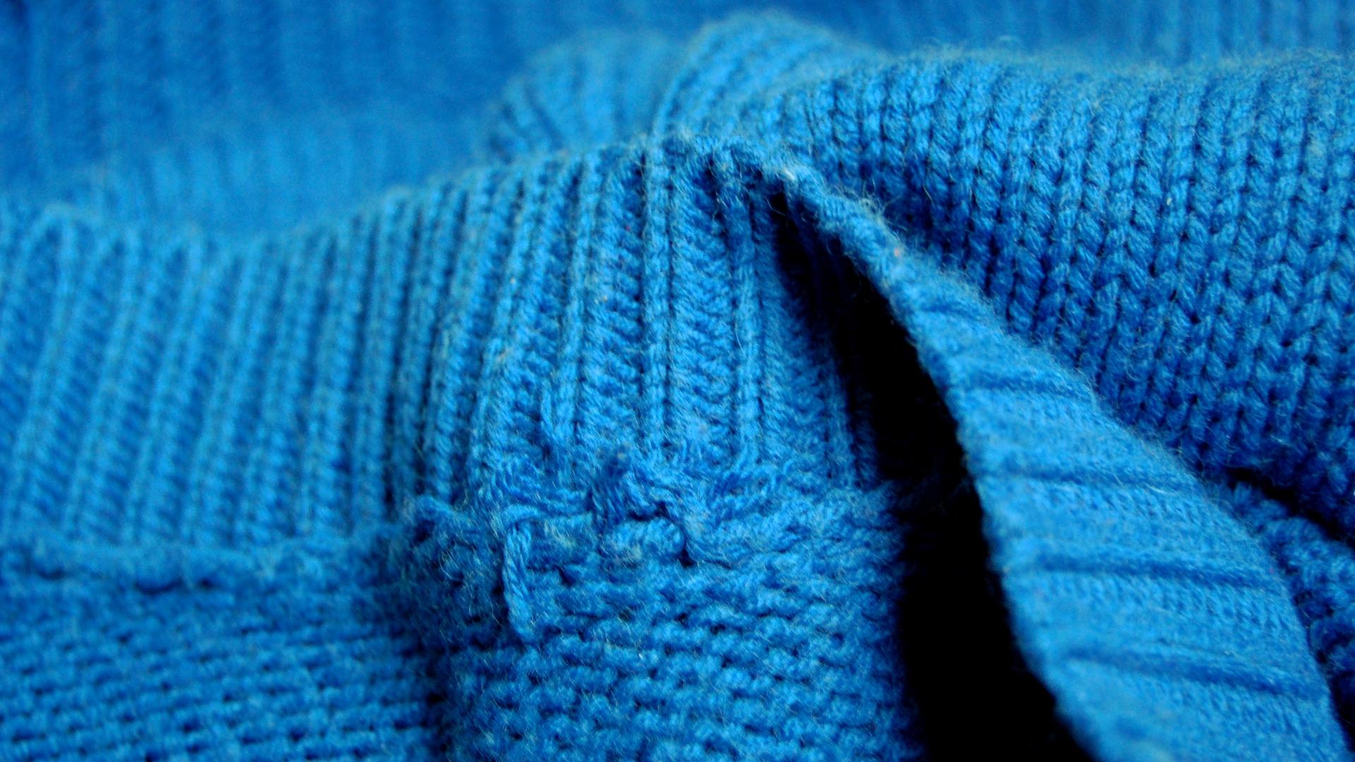 Ein blauer Strickpullover liegt in Falten im Bild.