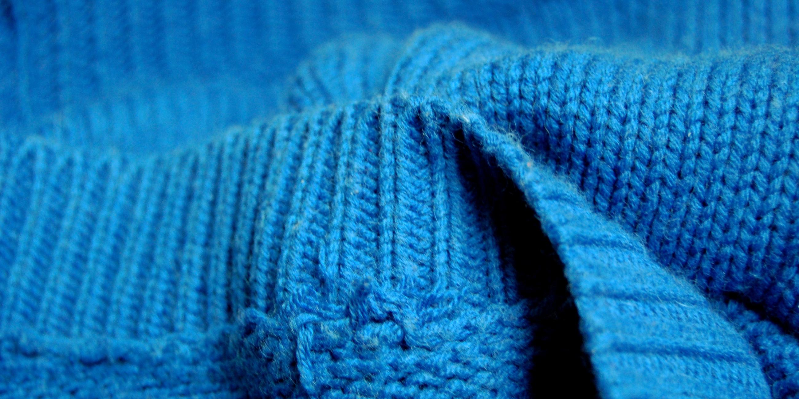 Ein blauer Strickpullover liegt in Falten im Bild.