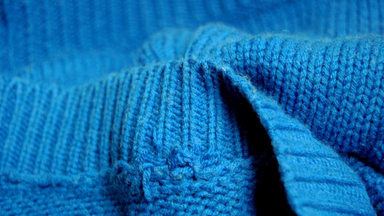 Ein blauer Strickpullover liegt in Falten im Bild.