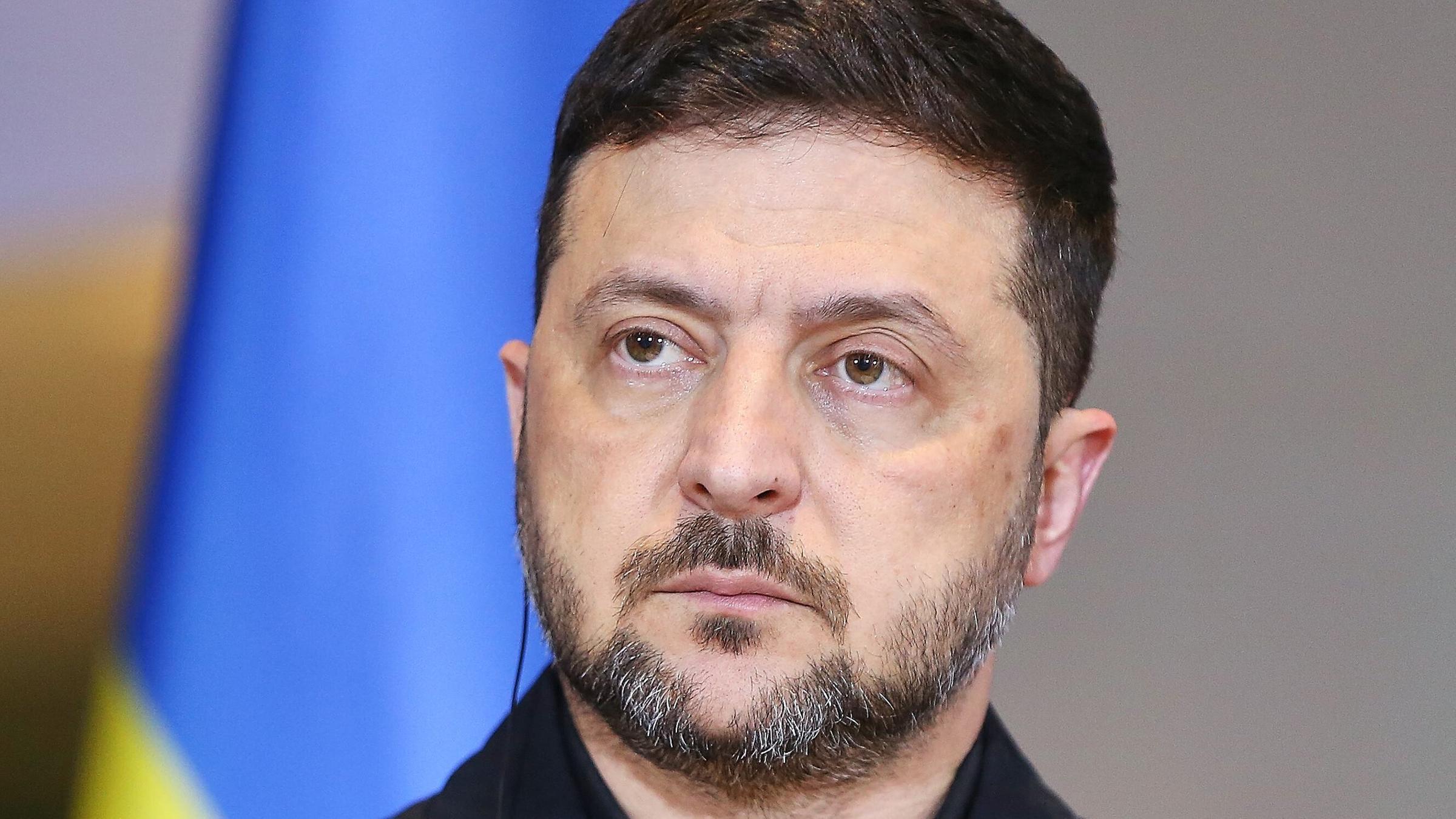 Ukraines Präsident Wolodymyr Selenskyj vor einer abgeschnittenen Fahne der Ukraine.