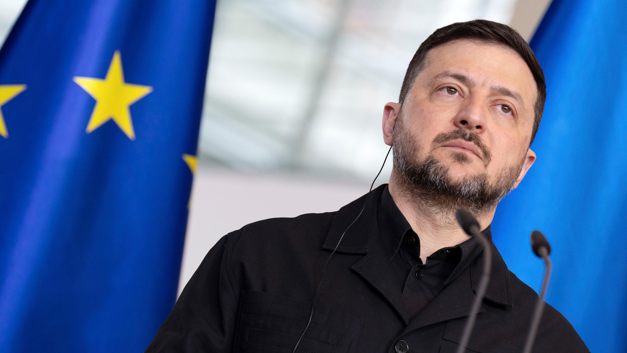 Wolodymyr Selenskyj steht vor einem Mikrofon-Pult. Im Hintergrund ist due Flagge der Europäischen Union zusehen.