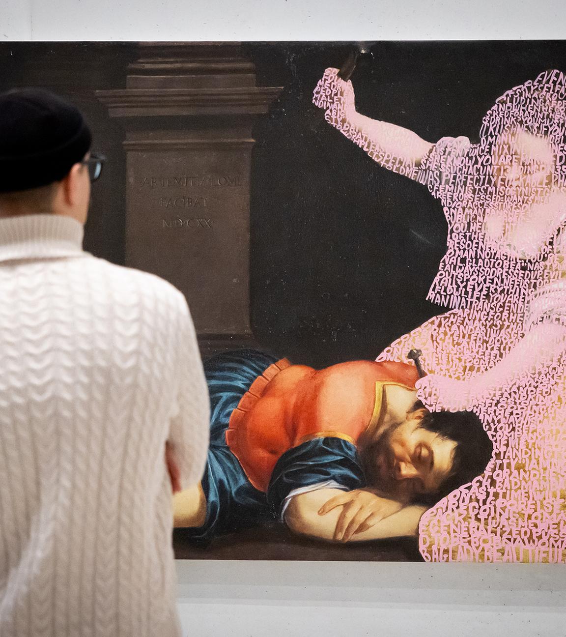 Ein Paar schaut sich ein großformatiges Bild an, auf dem ein Mann in historischer Kleidung schlafend auf dem Boden liegt, während eine Frau, die nur als verwitterter Umriss zu sehen ist, über ihm kniet und mit einer Hand ausholt.