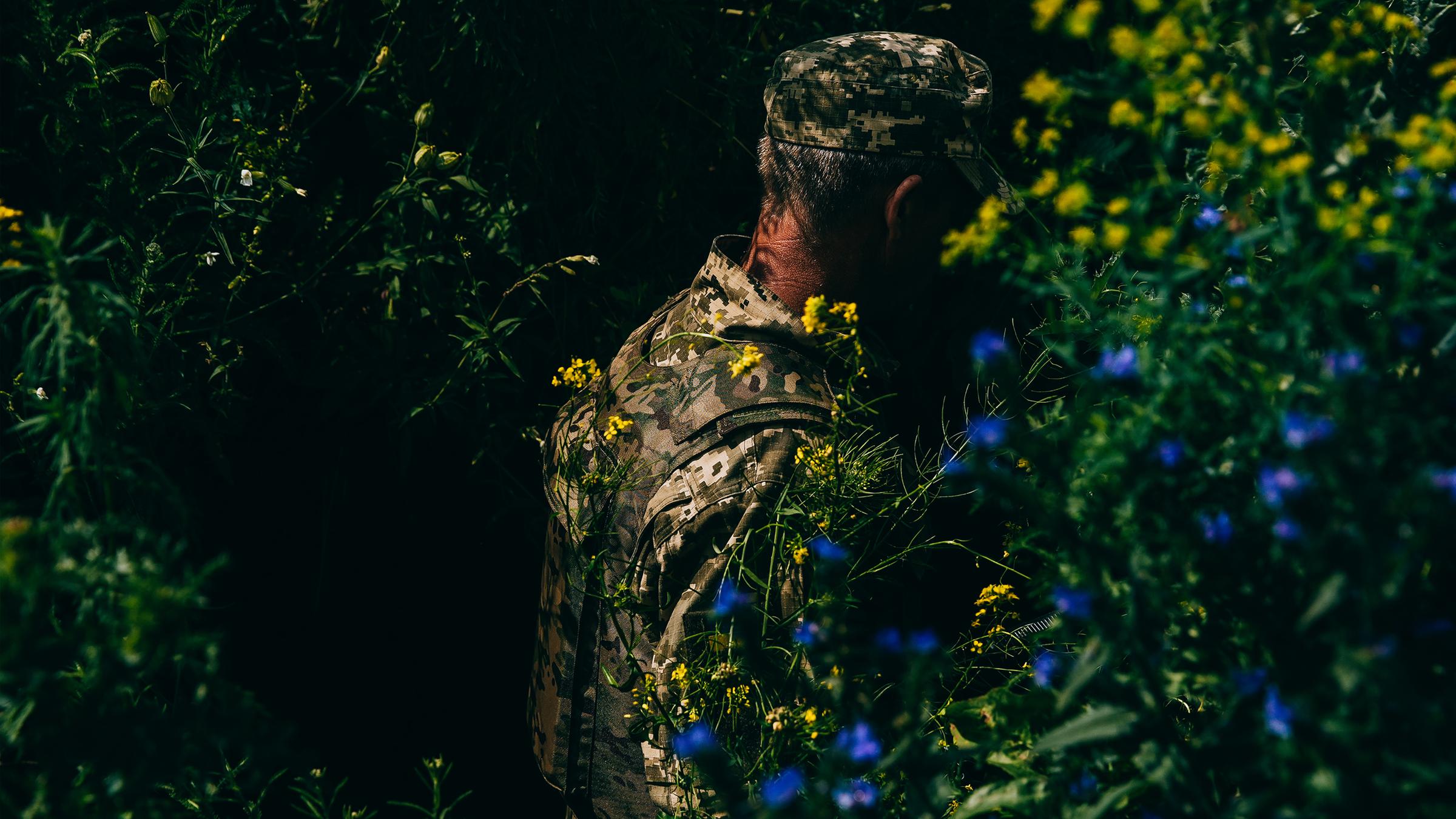 Ein ukrainischer Soldat steht in einem Gebüsch mit blühenden Sträuchern.
