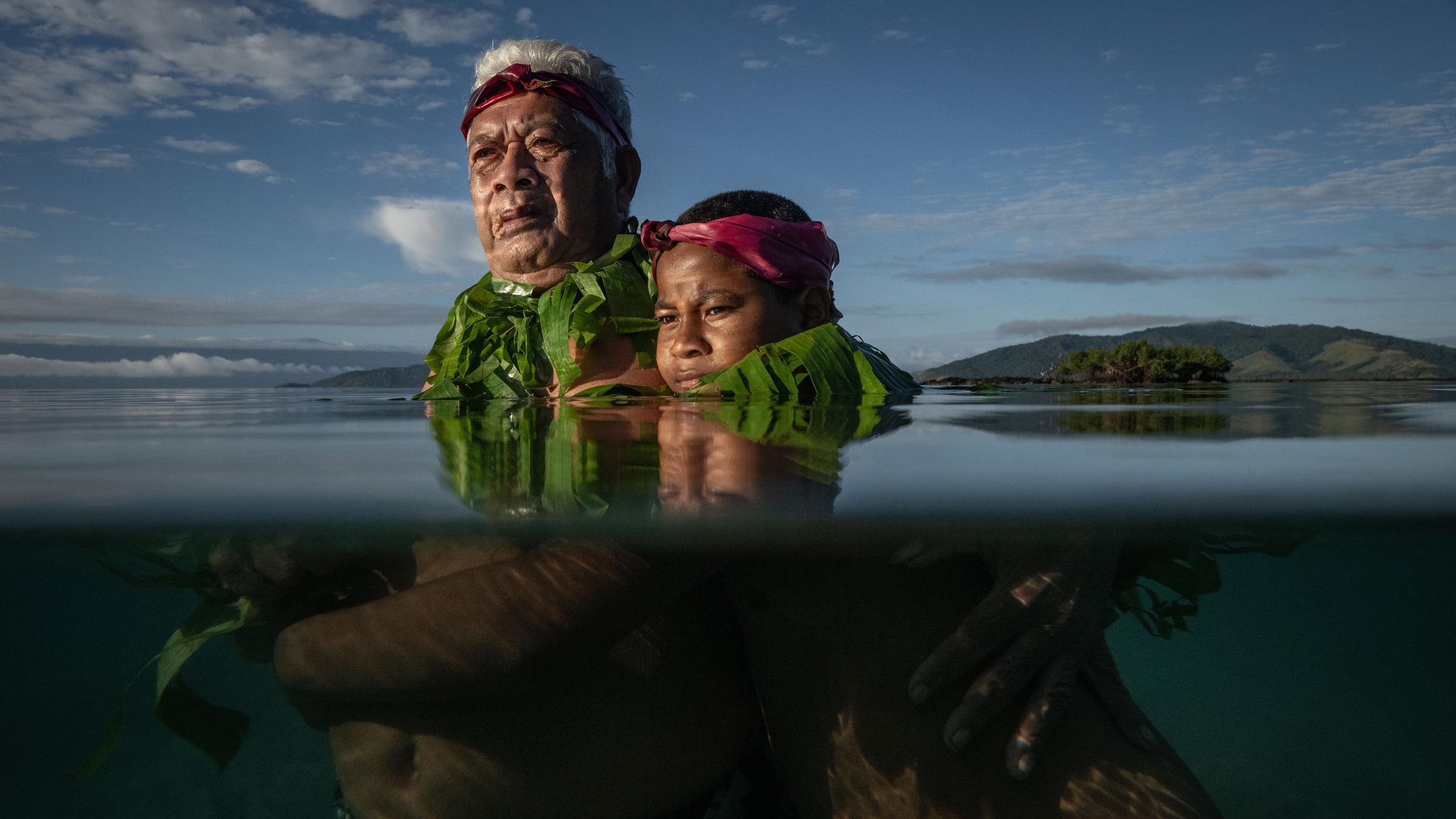 Lotomau Fiafia (72), a community elder, stands with his grandson John at the point where he remembers the shoreline used to be when he was a boy. Salia Bay, Kioa Island, Fiji, 8 August 2023 