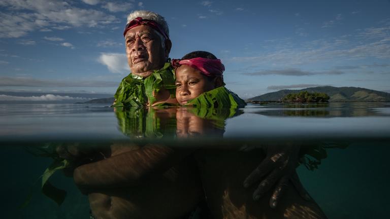 Lotomau Fiafia (72), a community elder, stands with his grandson John at the point where he remembers the shoreline used to be when he was a boy. Salia Bay, Kioa Island, Fiji, 8 August 2023 