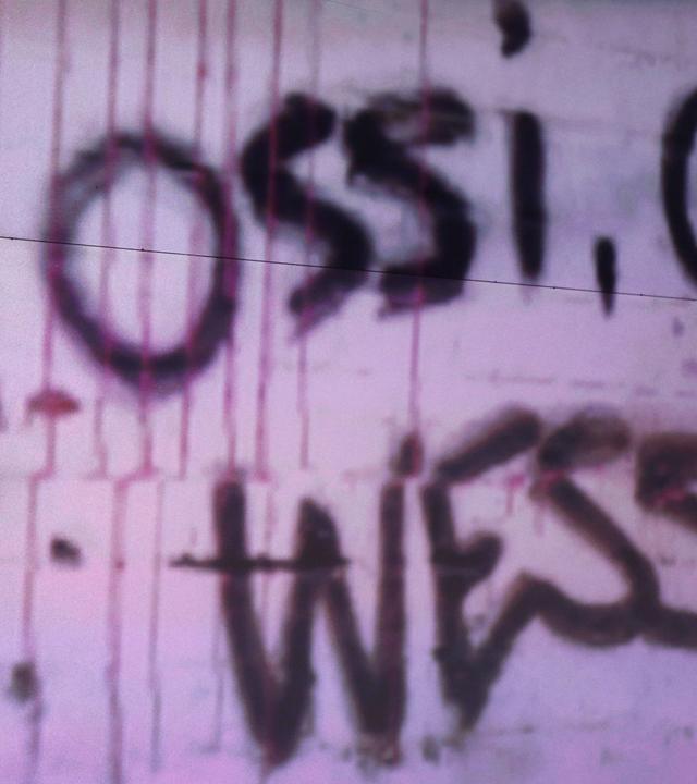 An einer Wand steht "OSSI ODER WESSI?", eine Studiodeko der ZDF-Talkshow "maybrit illner".