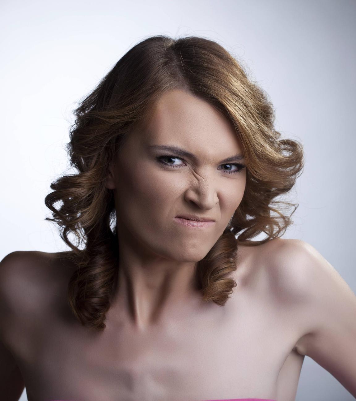 Eine junge Frau mit freiem Dekolleté ballt eine Faust und verzieht wütend das Gesicht.