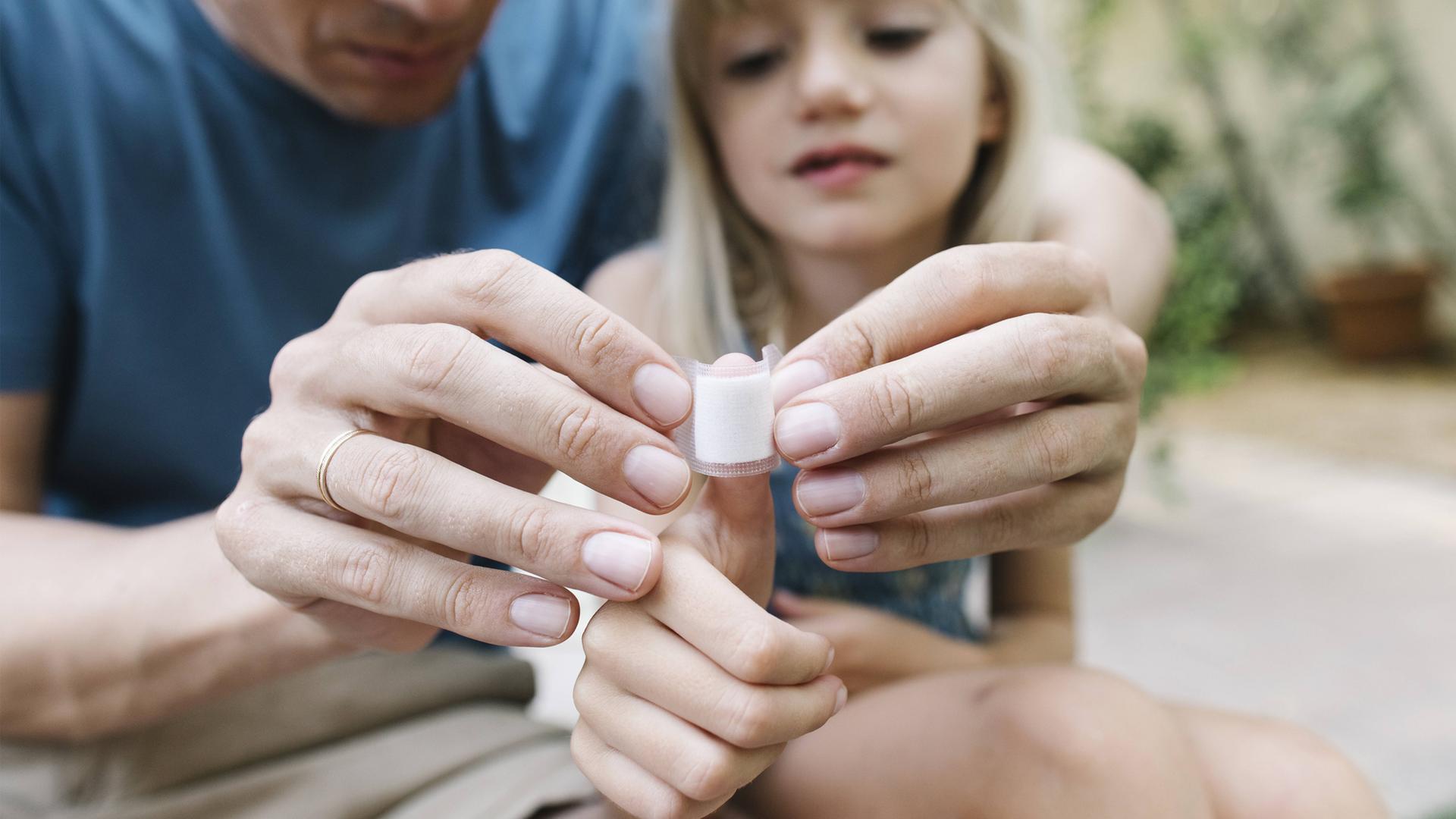 Ein Vater legt seiner Tochter einen Verband am Daumen an