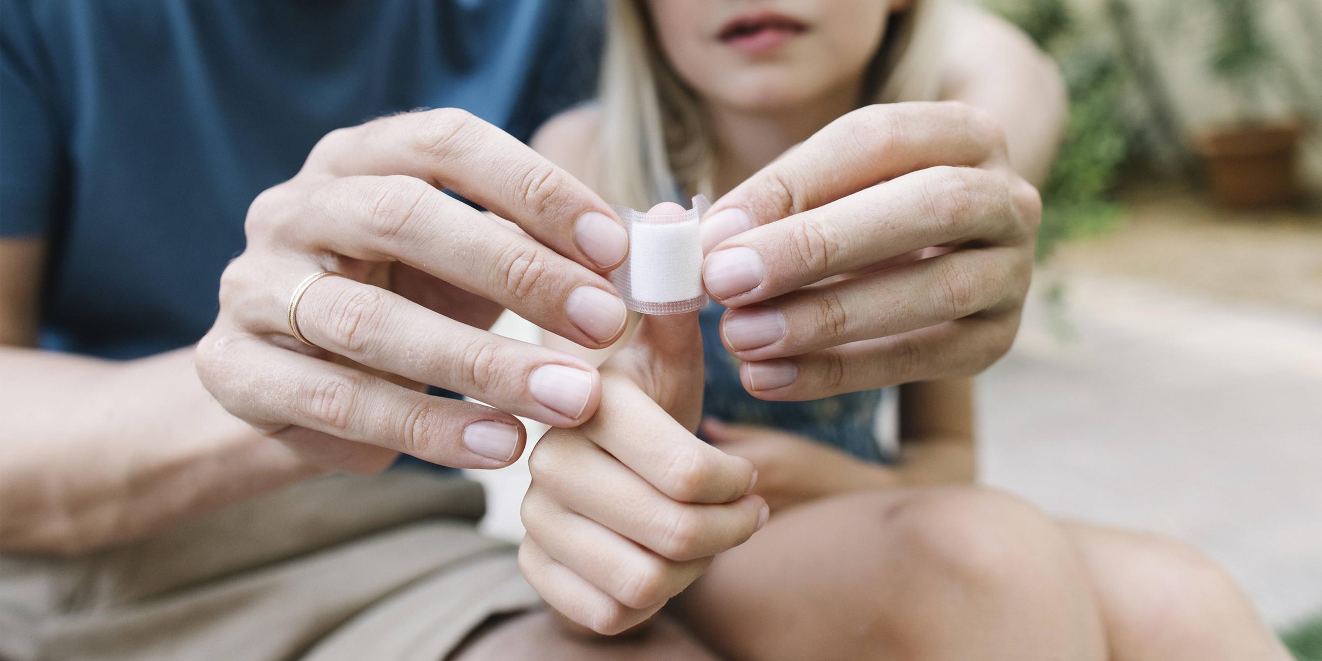 Ein Vater legt seiner Tochter einen Verband am Daumen an