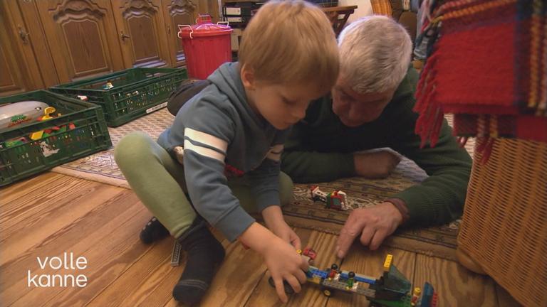 Wunschgroßvater und Junge spielen auf dem Boden mit Lego.