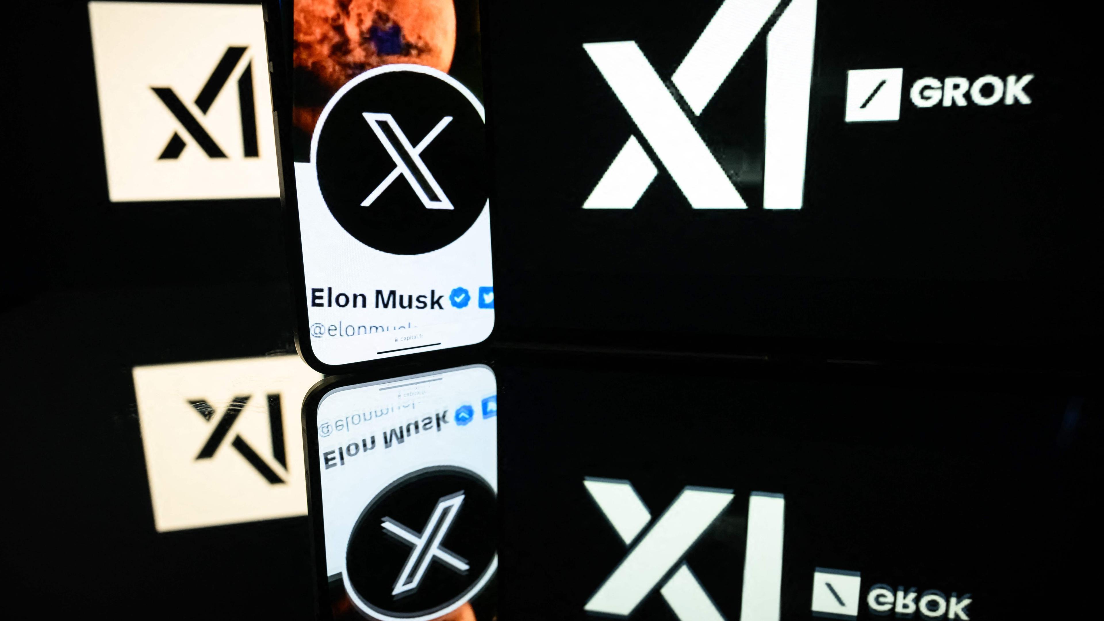 Bildschirme mit dem Logo von Grok und ein Smartphone mit Elon Musks X-Konto