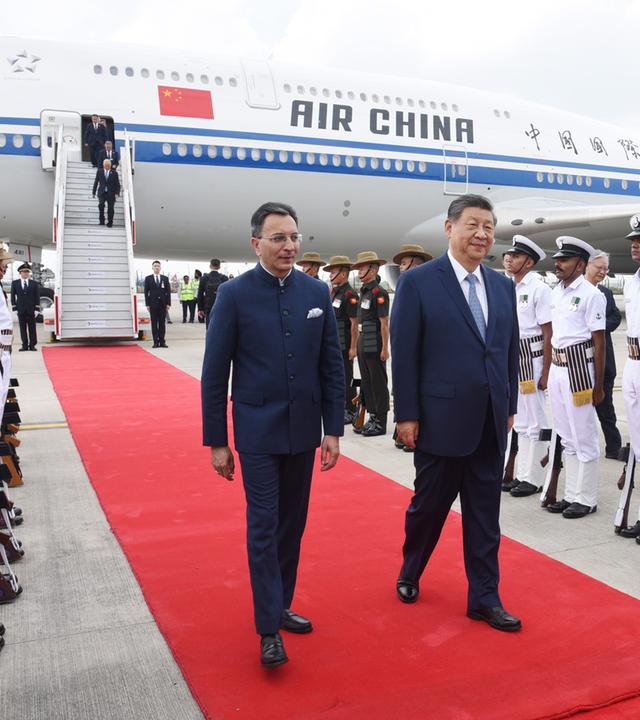 Der chinesische Präsident Xi Jinping läuft auf einem roten Teppich, im Hintergrund ist ein Flugzeug von Air China zu sehen.