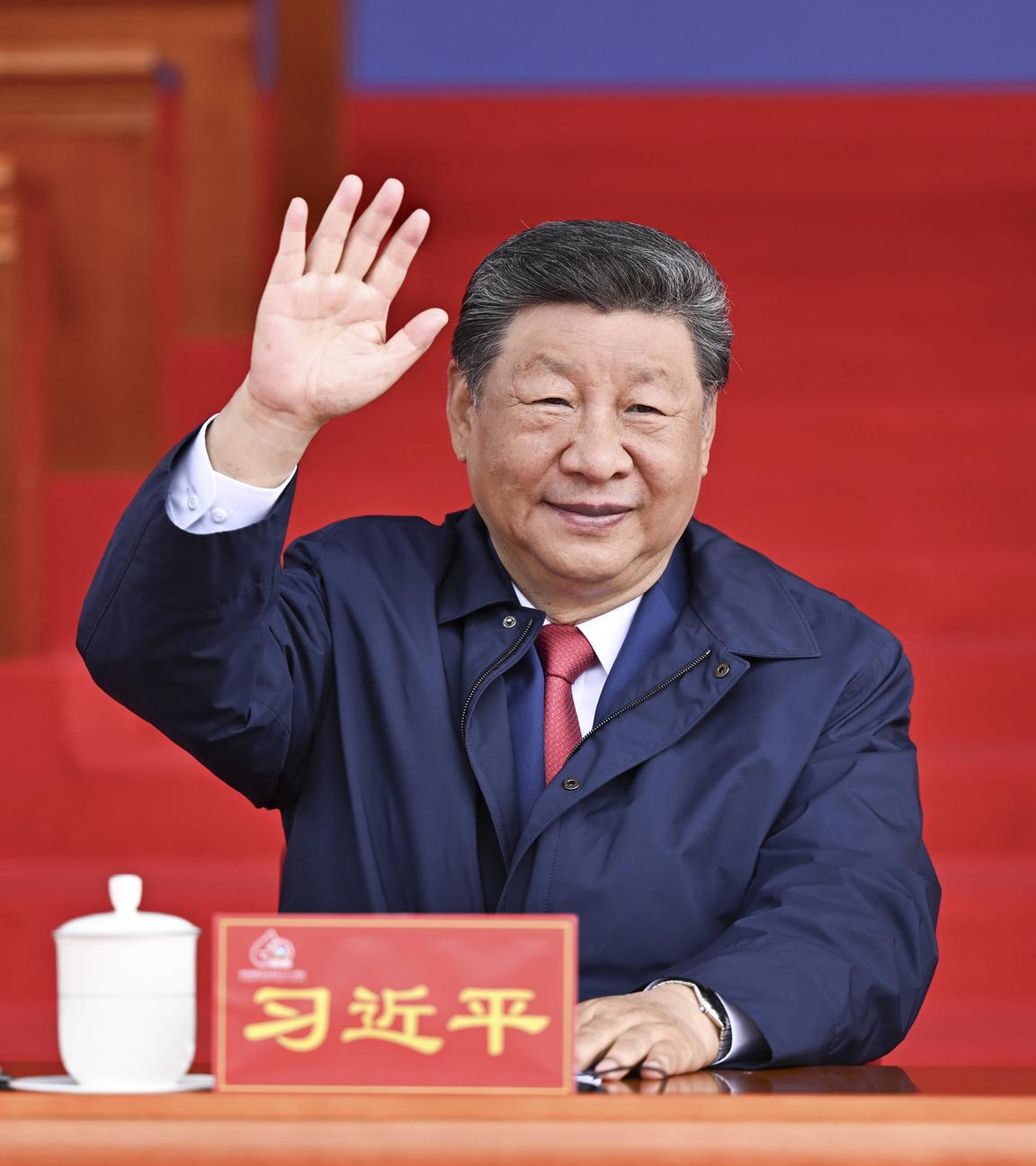 Xi Jinping sitzt und winkt in die Kamera.