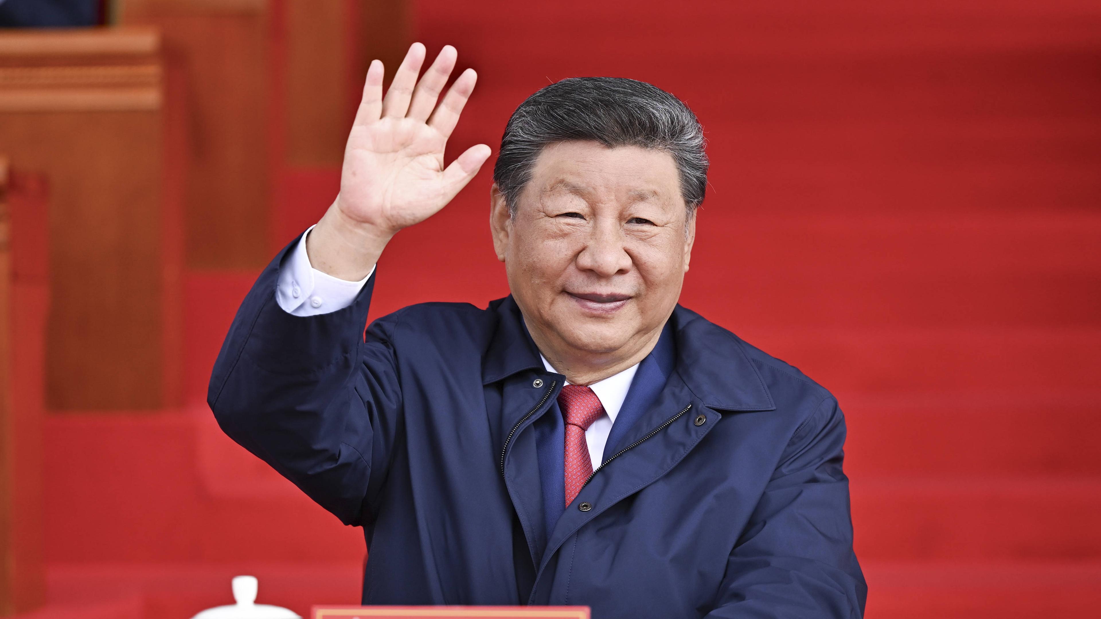 Xi Jinping sitzt und winkt in die Kamera.