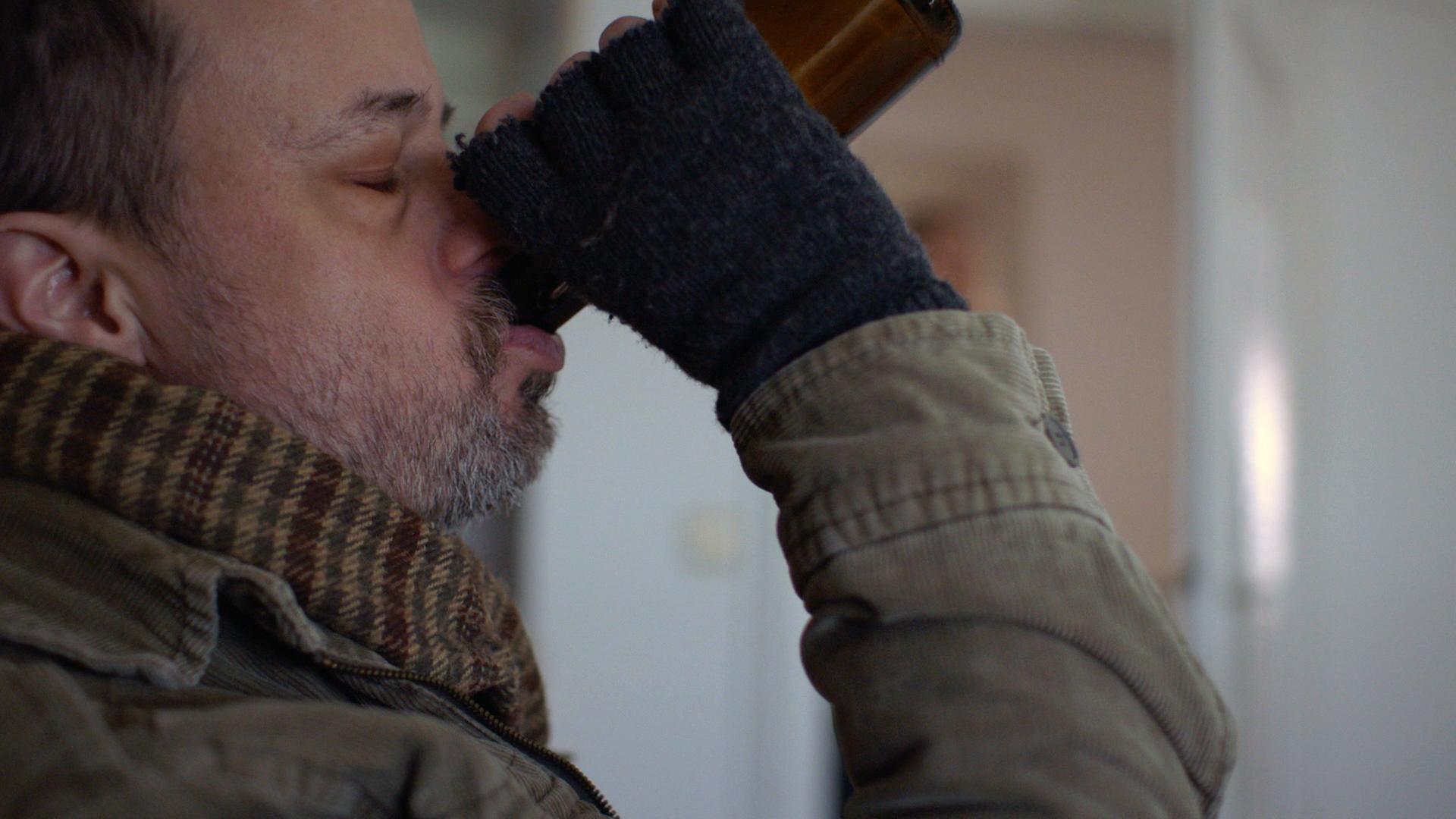 Nachgestellte Szene: Ein obdachloser Mann trinkt aus einer Flasche Bier.