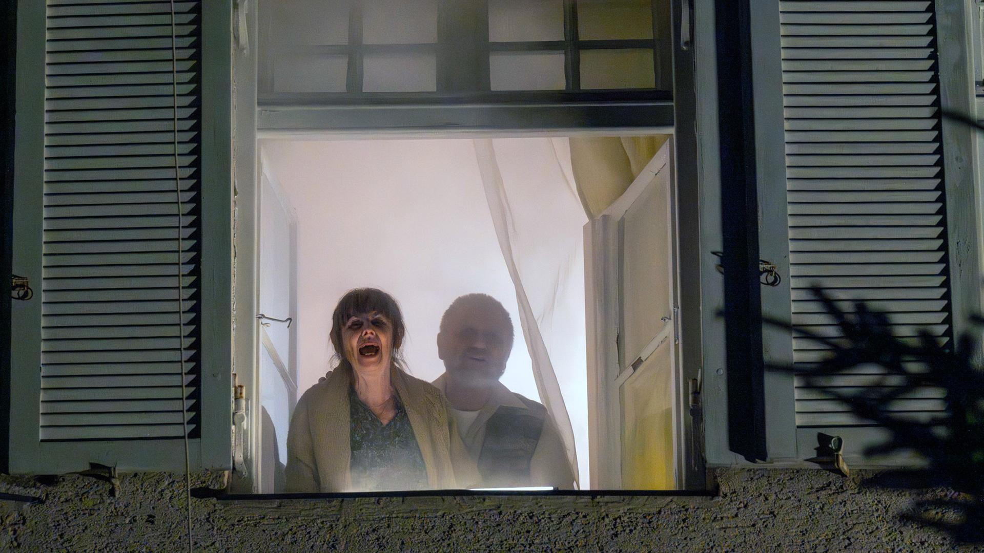 Nachgestellte Szene: Ein älteres Ehepaar steht am Fenster und ruft um Hilfe, während um sie herum das Haus brennt.